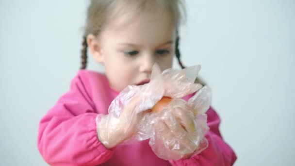 Wielkanoc, Pascha, dzieciństwo, kreatywność, koncepcja gier - zbliżenie małej uroczej blondynki trzyletniej dziewczyny ze Słowenii kaukaskiej wygląd w różowym szlafroku farby Pisanki w plastikowych rękawiczkach. — Wideo stockowe
