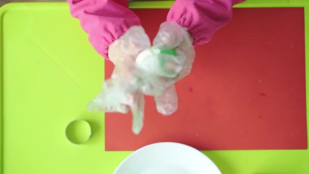 イースター、過越、子供時代、創造性、ゲームのコンセプト-ピンクのドレッシングガウンにスロベニアの白人の外観の小さなかわいいブロンドの3歳の女の子のクローズアップは、プラスチック製の手袋でイースターエッグをペイント. — ストック動画