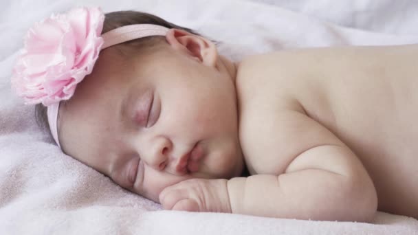 Kojenectví, dětství, vývoj, medicína a koncept zdraví - zblízka tvář novorozeně nahé spící holčičky ležící na břiše s obvazem a květinou na hlavě na růžovém pozadí. — Stock video