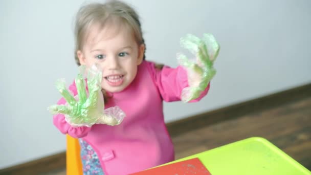 Pascua, Pascua, infancia, creatividad, concepto de juegos - primer plano de la pequeña rubia de tres años de edad, niña de aspecto caucásico esloveno en bata rosa pinta huevos de Pascua en guantes de plástico. — Vídeos de Stock