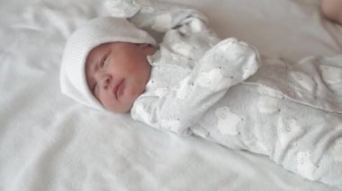 bebeklik, çocukluk, gelişim, tıp ve sağlık konsepti - bebek tulumu giymiş, beyaz bej arka planda sırtüstü uzanan bebek uykusundan uyanmış bebek için yakın çekim görüntüsü