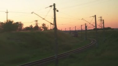 Ulaşım, seyahat, yol, demiryolu, manzara, çiftleşme konsepti - yaz aylarında günbatımından önce çayırların ve ormanların manzarasında cam ve paralel raylar üzerinde parlayan hız treninin penceresinden görünüm