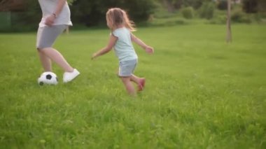 Çocukluk, oyunlar ve eğlence, spor, fiziksel kültür, parklar ve açık hava konsepti - küçük çocuklar ve anneleri güneş batarken parktaki yeşil çimlerde siyah ve beyaz topla futbol oynuyorlar..