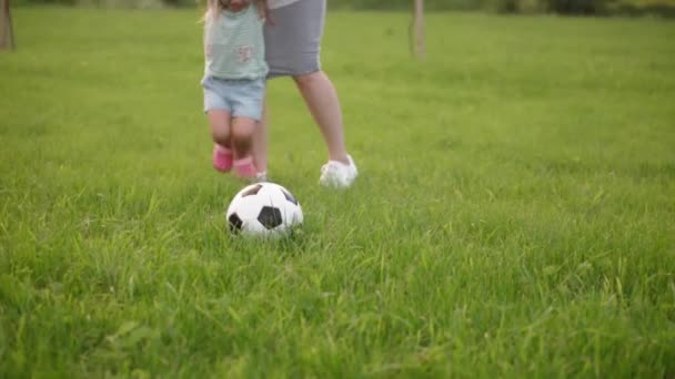 Kindheit, Spiel und Unterhaltung, Sport, Körperkultur, Parks und Open-Air-Konzept - kleine Jungen und Mädchen mit Mama spielen Fußball mit schwarz-weißem Ball auf grünem Rasen im Park bei Sonnenuntergang. — Stockvideo