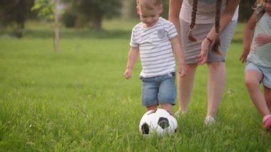 Çocukluk, oyunlar ve eğlence, spor, fiziksel kültür, parklar ve açık hava konsepti - küçük çocuklar ve anneleri güneş batarken parktaki yeşil çimlerde siyah ve beyaz topla futbol oynuyorlar..