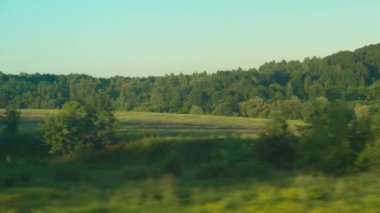 Ulaşım, seyahat, yol, demiryolu, manzara, yakınlaşma konsepti - yazın günbatımından önce çayırların ve ormanın güzel doğa sahalarının penceresinden hızlı trenin camına parlayan bakış