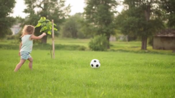 Infância, jogos e entretenimento, esportes, cultura física, parques e conceito ao ar livre - meninos e meninas crianças jogam futebol com bola preta e branca no gramado verde brilhante no parque ao pôr do sol — Vídeo de Stock