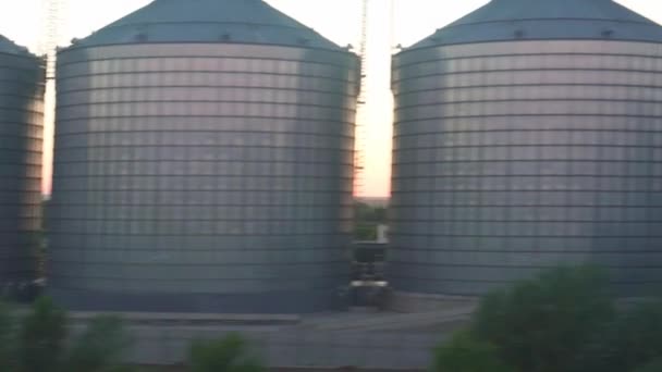 Transporte, viagens, estrada, ferrovia, paisagem, conceito de comnicação - vista da janela do trem de velocidade na paisagem de belo campo natural e silos de grãos de aço após o pôr do sol na noite de verão — Vídeo de Stock