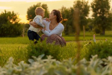 Annelik, bakım, bebekler, yaz, ebeveynlik konsepti - 2 yaşındaki oğlu olan güzel anne, gün batımında bahçede eğleniyor..