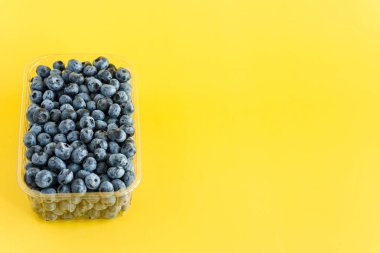 meyve ve yulaf, vitamin, sağlıklı yiyecek ve içecek, geleneksel tıp, gastronomi konsepti - parlak sarı arkaplan fotokopi alanı üzerinde plastik kömür tablasında mor ve mavi yaban mersini.