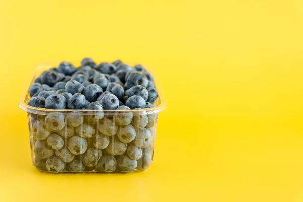 Fruit and oat, vitamin, healthy food and drink, traditional medicine, gastronomy concept - purple and blue blueberry berries in plastic charcoal transparent tray on bright yellow background copy space — Stock Photo, Image