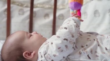 bebeklik, çocukluk, gelişim, tıp ve sağlık konsepti - yeni doğmuş çıplak, canlı, şakacı bebek suratları beyaz arka plandaki beşiğinde uzanan oyuncaklara uzanır