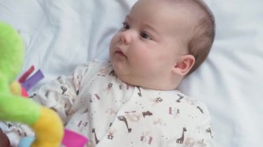 bebeklik, çocukluk, gelişim, tıp ve sağlık konsepti - yeni doğmuş çıplak, uyanık, neşeli bebek buruşuklukları beyaz arka plandaki beşikte uzanan oyuncaklara uzanır