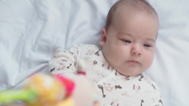 bebeklik, çocukluk, gelişim, tıp ve sağlık konsepti - yeni doğmuş çıplak, uyanık, neşeli bebek buruşuklukları beyaz arka plandaki beşikte uzanan oyuncaklara uzanır