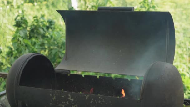 Кулинария, восточная кухня, лесные пожары, концепция поджога - зажигание огня и угля в черном металлическом гриле для курения и жарки мяса и овощной пищи в жару внешней дикой природы с дымом. — стоковое видео