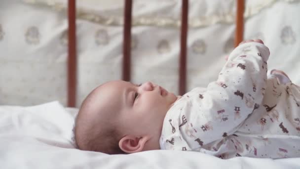 Niemowlęctwo, dzieciństwo, rozwój, medycyna i koncepcja zdrowotna - widok z bliska twarzy noworodka nago obudzony żywy zabawy grimaces baby sięgnąć po zabawkę leżącą na plecach w łóżeczku na białym tle — Wideo stockowe