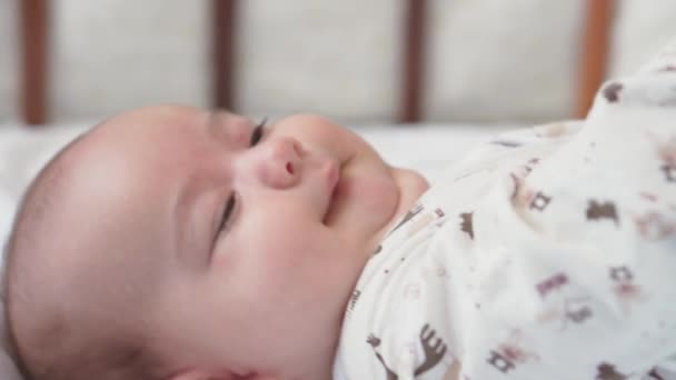 Βρεφική ηλικία, την παιδική ηλικία, την ανάπτυξη, την ιατρική και την υγεία έννοια - close-up όψη πλευρά του νεογέννητου γυμνό ξύπνιο ζωηρό παιχνιδιάρικο μωρό γκριμάτσες φτάσει για το παιχνίδι που βρίσκεται πίσω στην κούνια σε λευκό φόντο — Αρχείο Βίντεο