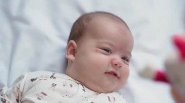 bebeklik, çocukluk, gelişim, tıp ve sağlık konsepti - yeni doğmuş çıplak, uyanık, neşeli bebek buruşuklukları beyaz arka plandaki beşikte uzanan oyuncaklara uzanır