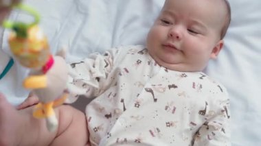 bebeklik, çocukluk, gelişim, tıp ve sağlık konsepti - yeni doğmuş çıplak, uyanık, neşeli bebek buruşuklukları beyaz arka plandaki beşikte uzanan oyuncaklara uzanır