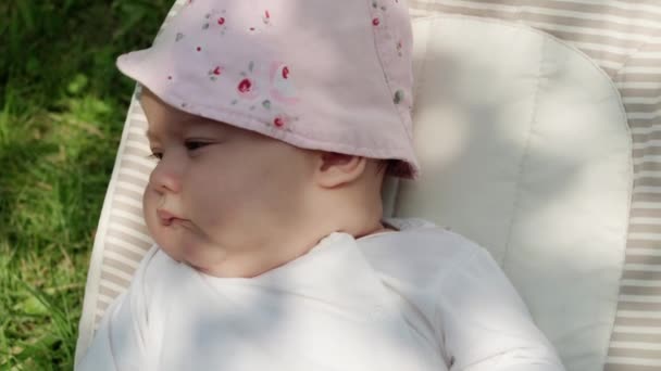 Copilăria, dezvoltarea, vacanța de vară, medicina și conceptul de sănătate - Portret de vedere de aproape al nou-născutului treaz fetiță de cinci luni situată pe fundalul scaunului balansoar de iarbă verde — Videoclip de stoc