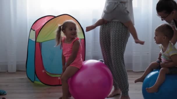 童年、母亲、游戏、抚养和发展的概念- -与年轻母亲同年龄的男孩和女孩在儿童游戏室高兴地跳起粉色的合球，微笑着 — 图库视频影像