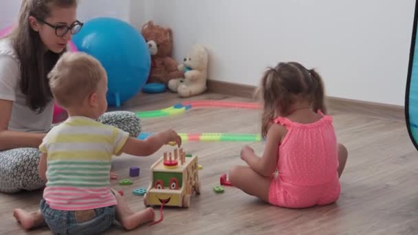 Childhood, games, upbringing and development concept - general plan of small children boy and girl of same age with mom are playing with childrens wooden car constructor and puzzles in kid playroom — Stock Video