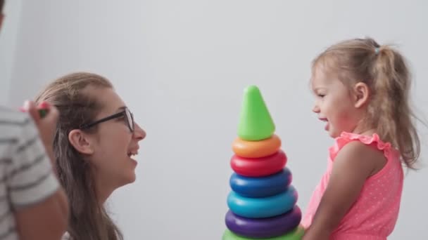 Dětství, hry, výchova a rozvoj koncepce - obecný plán malých dětí chlapec a dívka stejného věku s matkou hrají s pyramidou pestrobarevných prstenů duhových barev v dětském pokoji — Stock video