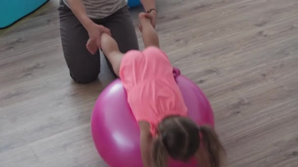 Barndom, morsrollen, spill, oppdragelses- og utviklingskonseptet - den generelle planen er at unge mamma med glede skal trene og spille masah med den lille treårige datteren på fitball og smile på barnerommet – stockvideo