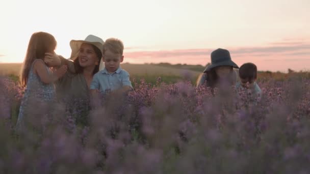 Groot gezin, vaderschap, kindertijd, moederschap, herkomststijl concept - Dekking schot twee jonge moeders verzamelen bloemen met kleine kinderen dochter en zoon op lavendelveld op de zomeravond voor zonsondergang — Stockvideo