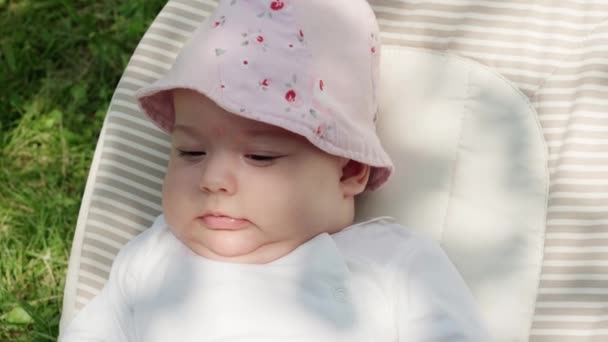 Младенчество, детство, развитие, летний отдых, медицина и концепция здоровья - Крупный план портрет бодрствующей новорожденной девочки в возрасте пяти месяцев, лежащей в кресле-качалке на фоне зеленой травы — стоковое видео