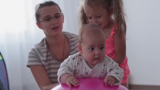 Infanzia, maternità, giochi, educazione e sviluppo concetto - close-up giovane mamma stanno facendo con gioia esercizio e masah con due neonati e figlie piccole su fitball e sorridente in sala giochi per bambini — Video Stock