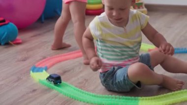 Çocukluk, oyunlar, yetiştirme ve geliştirme konsepti - küçük çocukların genel planı aynı yaşta erkek ve kız çocuklarının oyun odasında oyuncak motorlu arabalarla yarış pisti yapımcılarıyla oynuyorlar.