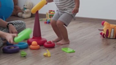 Çocukluk, oyunlar, yetiştirilme ve gelişim konsepti - annesiyle aynı yaşta küçük çocukların genel planı çocuk oyun odasında gökkuşağı renginde çok renkli halkalar piramidiyle oynuyor