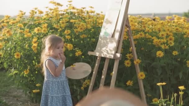 Infância, conceito de estilo de provence - pequeno 2 crianças menino e menina loira em vestido azul e chapéu de palha desenha no cavalete perto do arbusto de crisântemos amarelos campo de lavanda na noite de verão antes do pôr do sol — Vídeo de Stock