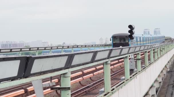 Transportul public urban, călătoriile, infrastructura, conceptul metropolei - un tren de metrou albastru și galben trece printr-o stație de la sol pe un pod peste râul Nipru . — Videoclip de stoc