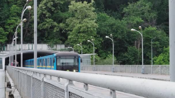 Trasporto pubblico urbano, viaggi, infrastrutture, concetto di metropoli: un treno blu e giallo passa attraverso una stazione di terra su un ponte sul fiume Dnieper. — Video Stock