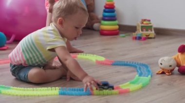 Çocukluk, oyunlar, yetiştirme ve geliştirme konsepti - küçük çocukların genel planı aynı yaşta erkek ve kız çocuklarının oyun odasında oyuncak motorlu arabalarla yarış pisti yapımcılarıyla oynuyorlar.