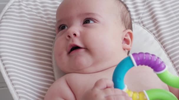 Bebeklik, çocukluk, gelişim, yaz tatili, tıp ve sağlık konsepti - 5 aylık uyanık bebek bebek portresinin yakın çekimi oyuncak teether ile dışarıda sallanan sandalyede yatıyor — Stok video
