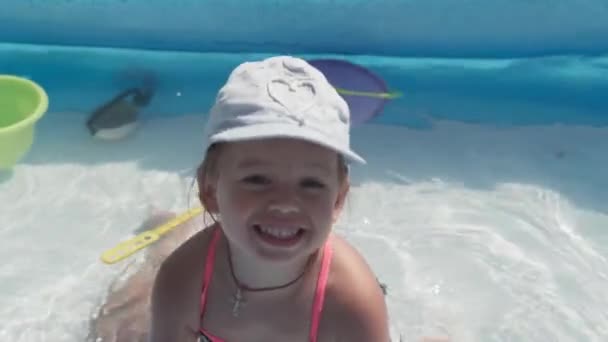 Küçük mutlu 3 yaşındaki mavi şapkalı ve mayo giyen Avrupalı Slav görünümlü bir kız yazın bilardo oynuyor, su sıçratıyor, yaşam tarzı tasarımı yapıyor. Aktivite doğa eğlencesi. Yavaş çekim — Stok video