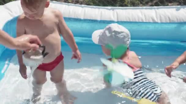 Dvě malé děti chlapec a dívka kavkazský evropský slovanský vzhled ve stejném věku jsou šťastný koupel a hýčkat v bazénu v létě, stříkající vody, životní styl designu. Činnost příroda volný čas. Zpomalený pohyb — Stock video