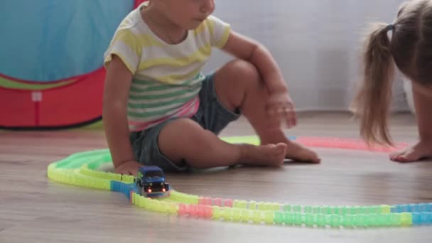 童年、游戏、抚养和发展的概念- -同龄男女幼儿的总体规划- -在儿童游戏室内与玩具车的赛车场建设者玩耍. — 图库视频影像