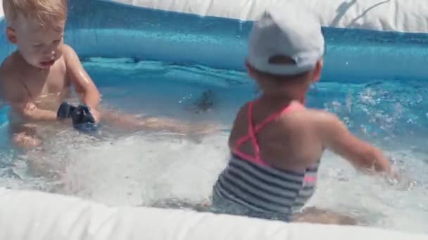 Zwei kleine Kinder Jungen und Mädchen kaukasischen europäisch-slawischen Aussehens gleichen Alters sind glücklich baden und toben im Pool im Sommer, plätscherndes Wasser, Lifestyle-Design. Aktivität Natur Freizeit. Zeitlupe — Stockvideo