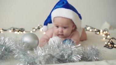 Mutlu noeller ve mutlu yıllar, bebekler, çocukluk, tatil konsepti - yakın plan çıplak bebek Noel Baba şapkalı 6 aylık bebek Noel Baba 'nın karnında Noel ağacı süslemeleri ile sürünüyor.