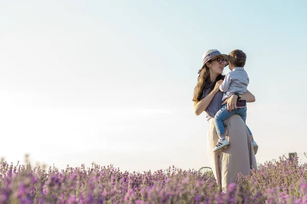 Large family, fatherhood, childhood, motherhood, provence style concept - happy young mom with little kid boy son of Middle Eastern appearance holds in arms on lavender field on summer before sunset