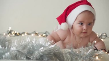 Mutlu noeller ve mutlu yıllar, bebekler, çocukluk, tatil konsepti - yakın plan çıplak bebek Noel Baba şapkalı 6 aylık bebek Noel Baba 'nın karnında Noel ağacı süslemeleri ile sürünüyor.
