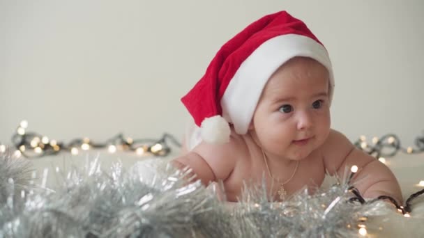 Feliz Navidad y feliz año nuevo, bebés, infancia, concepto de vacaciones - primer plano desnudo bebé recién nacido de 6 meses en sombrero de Santa Claus en su barriga se arrastra con decoraciones en el árbol de Navidad. — Vídeo de stock