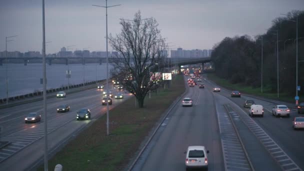 Kijów, Ukraina -18.05.2020: plan ogólny widok z lotu ptaka autostrady z wielu samochodów osobowych i ciężarowych w pobliżu szerokiej rzeki Dniepr wieczorem. transport, komunikacja, infrastruktura, koncepcja urbanizacji — Wideo stockowe