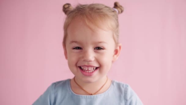 Childhood, celebration, birthday, games concept - close-up happy little blond-haired girl in blue dress looking at camera covers ears screams and showing different emotions on pink solid background. — Stock Video