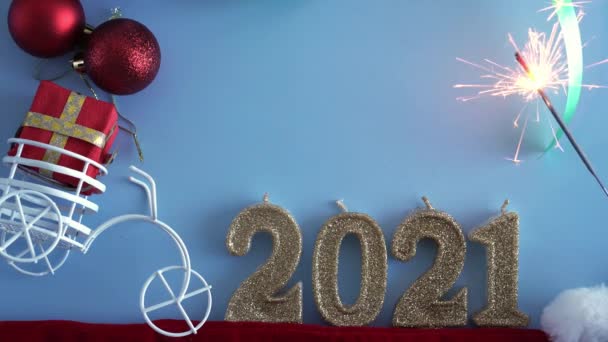 Xmas, зима, щаслива нова концепція року - синій різдвяний фон з номером 2021 номер золотих свічок і іграшкового велосипеда з подарунком в багажнику і палаючим ігриком. Прямо, вгорі, над головою. Копіювальний простір — стокове відео