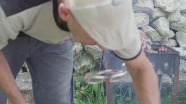 Yemek pişirmek, piknik yapmak, oryantal mutfak konsepti şort giyen, baltayla odun kesen ve açık havada ateşe atan son sınıf öğrencisinin yakın çekimi. Taşların ızgara arka planında et ve sebze içmek